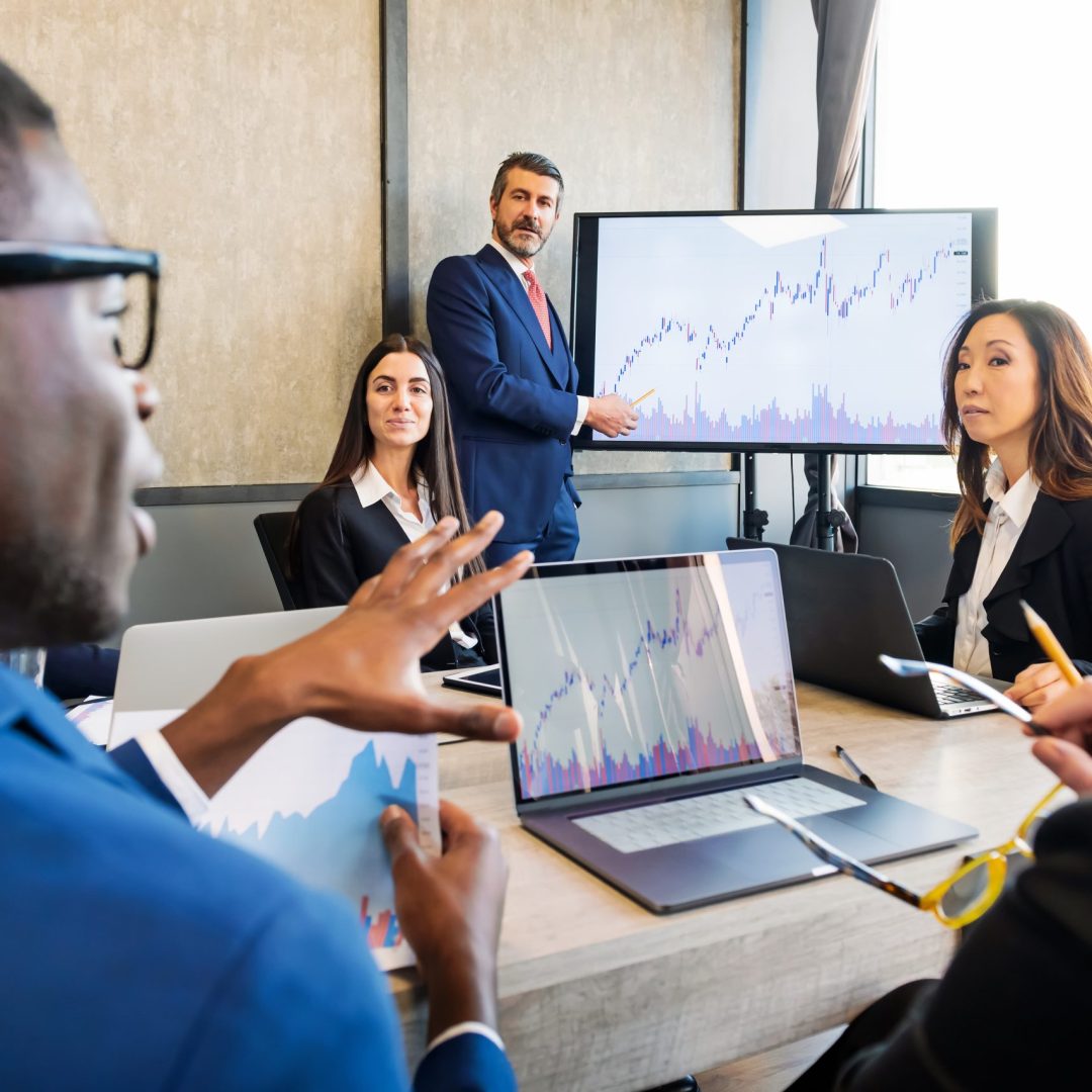 Group of multiethnic colleagues in formal wear gathering at table with laptops while discussing financial business project during presentation